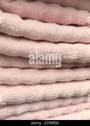 I morbidi asciugamani rosa pastello sono impilati ordinatamente, creando un ambiente caldo e invitante in un bagno. La loro consistenza lussuosa suggerisce comfort e rela Foto Stock