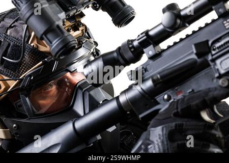 Operatore tattico mirato che punta il proprio fucile dotato di oscilloscopi, con casco da combattimento avanzato e occhiali di protezione, e con equipaggiamento militare professionale A. Foto Stock