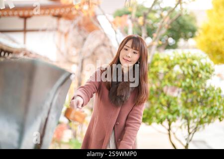 Un santuario a Hakata, Fukuoka, Giappone. Una donna giapponese con i capelli lunghi sui trent'anni pulisce le mani usando un mestolo. Foto Stock