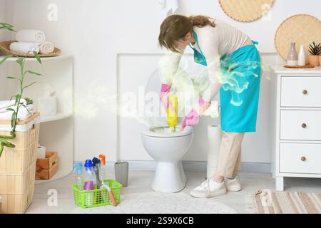 Giovane donna che pulisce la ciotola sporca del bagno in bagno Foto Stock