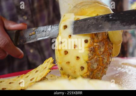 Sbucciare l'ananas in un vivace mercato al mattino Foto Stock