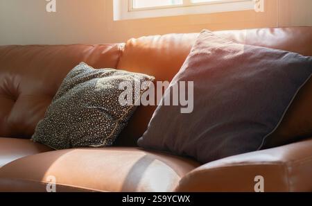 Comodi divani e cuscini in pelle arancione con una luce soffusa del sole proveniente dalla finestra posteriore. Concetto di stile di vita. Foto Stock