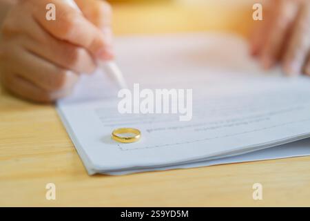 Mani di moglie, marito che firma il decreto di divorzio, che annulla il matrimonio o l'accordo prematrimoniale redatto dall'avvocato. Messa a fuoco selettiva sull'anello. Foto Stock