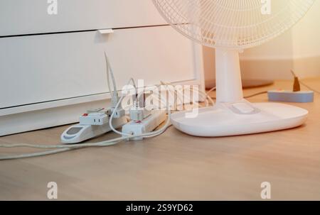 Schede di alimentazione sovraccaricate con ventola elettrica su pavimento in legno a casa. Messa a fuoco selettiva. Foto Stock