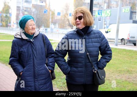 Due signore anziane, madre e figlia, che camminano per la città, parlano, ridono, bevono caffè. Stile di vita sano e attivo Foto Stock