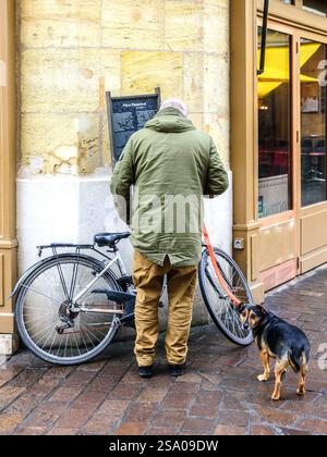 Vista posteriore dell'uomo che fissa la bicicletta tenendo un cane piccolo al guinzaglio - Tours, Indre-et-Loire (37), Francia. Foto Stock