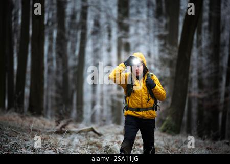 Escursioni nella foresta invernale. L'escursionista con faro cammina nel bosco durante il crepuscolo. Avventura nella natura Foto Stock