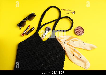Composizione piatta con sacchetto per la spesa in macrame e prodotti per il trucco su sfondo giallo Foto Stock