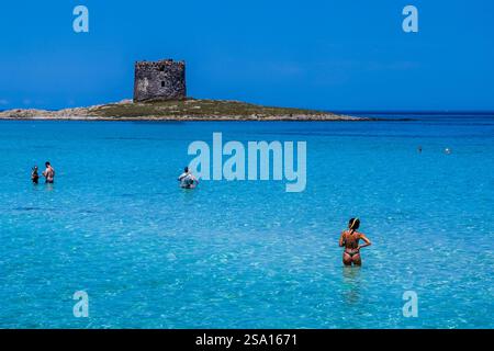 L'antica torre di avvistamento Torre della Pelosa sulla famosa spiaggia la Pelosa, che si trova sulla penisola di Stintino, persone in piedi in acque poco profonde. Foto Stock