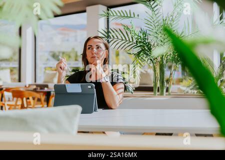 Una donna è seduta a un tavolo con un tablet di fronte a lei e ha un'espressione premurosa. Foto Stock