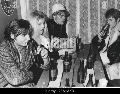 Negli anni '1960 Un gruppo di giovani che bevono birra e fumano. Niente bicchieri, solo bere dalle bottiglie di birra. Un'immagine che illustra alcune cose molto tipiche come la moda e l'aspetto delle persone negli anni '1960 1968 Foto Stock
