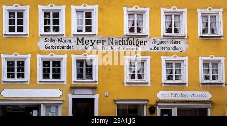 Una facciata di un edificio giallo vibrante caratterizzato da finestre multiple con cornici bianche. L'edificio mostra una vecchia segnaletica per un'azienda chiamata "Meyer Nachfolge" Foto Stock