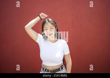 Donna asiatica che cresce han che danza K-pop danza contro un muro rosso sotto il sole Foto Stock