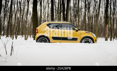 Vista laterale di Suzuki Ignis nella neve profonda. Guida crossover in SUV color senape nella foresta invernale innevata. Foto Stock