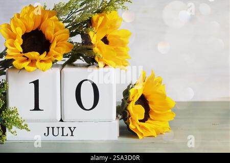 U. S. Energy Independence Day. Blocchi di calendario in legno bianco con la data del 10 luglio e bel bouquet di girasole con bokeh. Messa a fuoco selettiva. Foto Stock