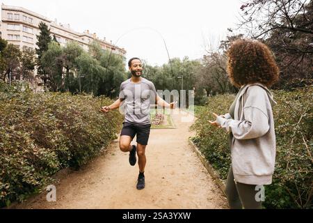 Un allenatore esegue un esercizio di salto di corda in un parco mentre la sua cliente femminile sta guardando. Foto Stock
