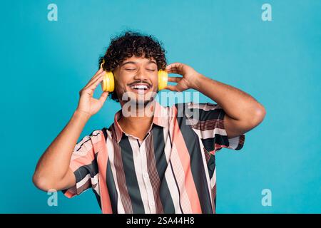 Foto di auricolari a righe eccentrici e cool, che cantano uno spazio in rilievo, sfondo blu isolato Foto Stock
