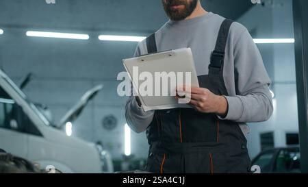 Caucasico uomo meccanico scrittura modulo fissaggio auto in auto servizio di manutenzione officina professionale maschio tecnico ingegnere automobilistico scrittura Foto Stock