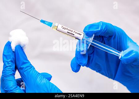 L'immagine mostra un medico che tiene in mano una siringa con il vaccino contro la febbre tifoide in mano, indossando guanti blu, e sullo sfondo c'è una donna anziana Foto Stock