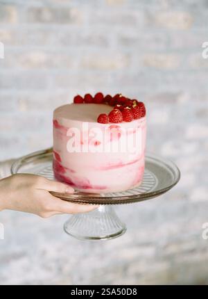 Bellissima torta a strati ricoperta di fragole fresche esposte su un supporto di vetro in un ambiente luminoso Foto Stock