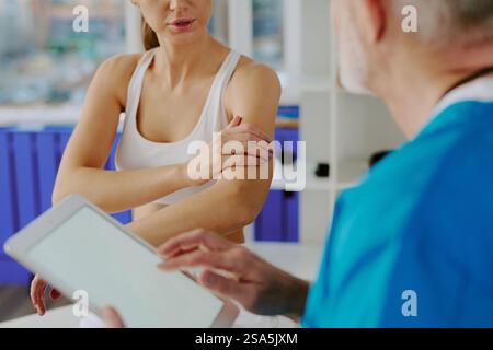 La vista a spalla di un medico irriconoscibile con l'ascolto di un tablet si lamenta del suo paziente che spiega la pittura in bicipite Foto Stock