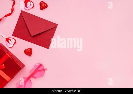 Pacchetto regalo di San Valentino colorato con busta rossa, caramelle e divertenti accessori su sfondo rosa Foto Stock