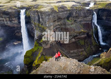 Maestosa vista aerea con drone in piedi per due persone in giacche rosse sopra le cascate Haifoss e Granni in Islanda, che si infrangono in un aspro canyon Foto Stock