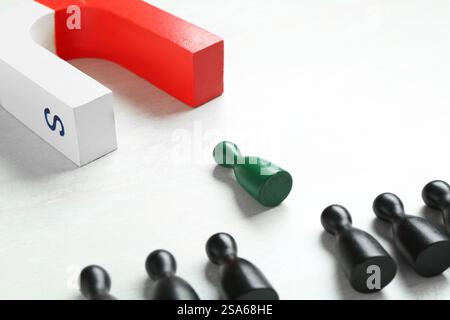 Calamita che attrae una pedina verde tra quelle nere sul tavolo bianco, primo piano Foto Stock