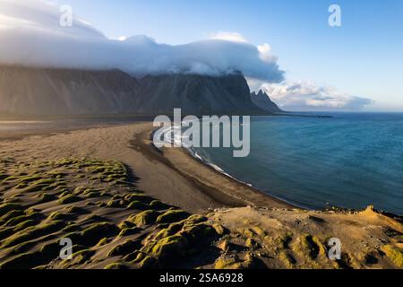 Un affascinante paesaggio costiero di Stokksnes in Islanda caratterizzato da una spiaggia di sabbia nera, dune lussureggianti, tramonto dorato, torreggianti montagne Vestrahorn, Atlantico Foto Stock