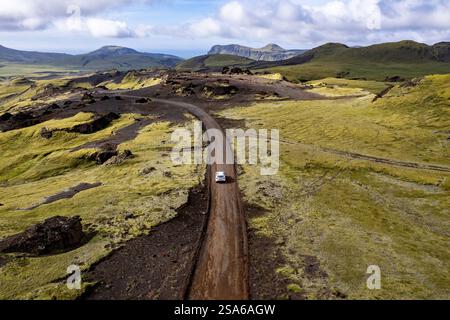Vista aerea con droni esplorando il paesaggio della valle con un'auto bianca solitaria 4x4 su una strada sterrata per il campeggio Thakgil (Pakgil) vicino a Vik in Islanda Foto Stock