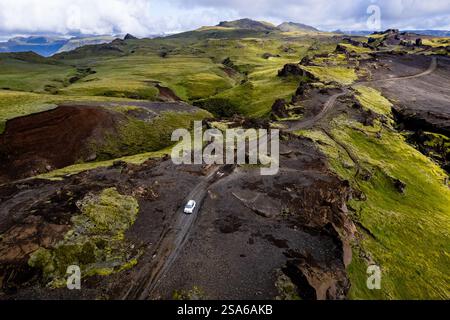 Vista aerea con droni esplorando il paesaggio della valle con un'auto bianca solitaria 4x4 su una strada sterrata per il campeggio Thakgil (Pakgil) vicino a Vik in Islanda Foto Stock