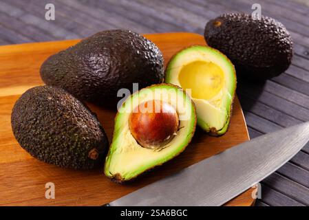 Avocado fresco intero e dimezzato su superficie di legno Foto Stock