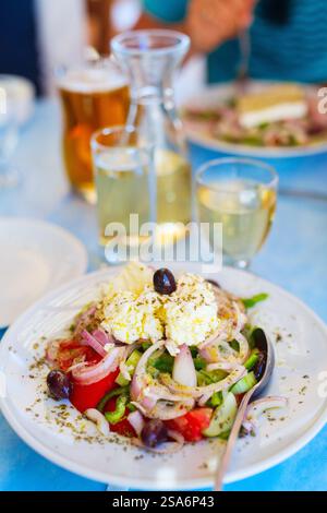 Deliziosa insalata greca con verdure fresche e formaggio greco feta di capra servito con vino bianco per pranzo al ristorante Foto Stock