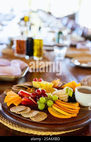 Un piatto ben organizzato con frutta fresca, formaggio, cracker e salse su un tavolo di legno per cenare, evocando un'atmosfera calda e invitante. Foto Stock