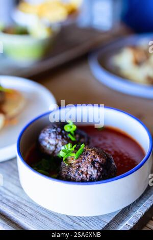 Polpette succose servite in una ricca salsa di pomodoro, guarnite con cipolle verdi fresche, collocate in una ciotola bianca con uno sfondo rustico da tavolo in legno. Foto Stock