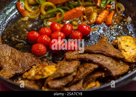 bistecca con cipolle, pomodori e peperoni preparati in una padella su un piano cottura a gas Foto Stock