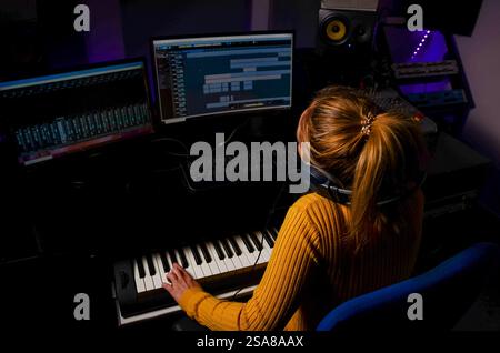 Produttore musicale femminile che compone musica utilizzando computer, tastiera e cuffie in uno studio di registrazione professionale Foto Stock