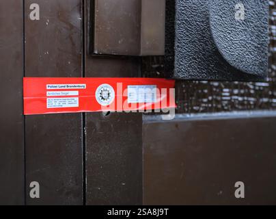 29 gennaio 2025, Brandeburgo, Francoforte (Oder): Un sigillo della polizia di Brandeburgo è attaccato alla porta d'ingresso di un condominio. Tre persone sono morte in un incendio in un appartamento a Francoforte (Oder). Questo è stato annunciato dai vigili del fuoco della città su richiesta. I servizi di emergenza sono stati allertati in tarda serata il martedì alle 22 circa. Diversi media avevano riferito in precedenza. Come riportò il "Märkische Oderzeitung", le fiamme sparavano già da una finestra del balcone quando arrivarono i servizi di emergenza. Durante i lavori di estinzione, un certo numero di altri residenti della casa sono stati presi Foto Stock