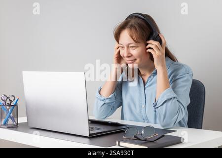 Allegra donna professionista freelance che indossa cuffie di grandi dimensioni che parla durante una chat online utilizzando il laptop, parla durante una videoconferenza, sorride, Foto Stock
