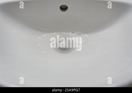 Vista dall'alto di un lavandino in ceramica del bagno con acqua che scorre attraverso lo scarico. Con spazio per copiare. Foto di alta qualità Foto Stock