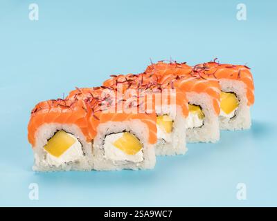 Fotografia in studio di Philadelphia Roll di vellutato formaggio spalmabile e mango avvolti in un perfetto sushi di riso stagionato e salmone fresco, microgreen decorati. Isolato su sfondo blu chiaro fisso Foto Stock