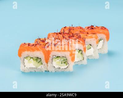 Fotografia in studio di Philadelphia Roll di vellutato formaggio spalmabile e cetriolo avvolto in perfetto sushi di riso stagionato e salmone fresco, microgreen decorati. Isolato su sfondo blu chiaro fisso Foto Stock