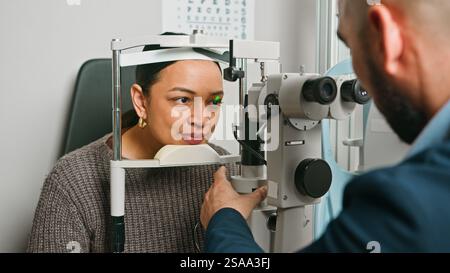 Optometrista esecuzione di esami oculistici per pazienti che utilizzano apparecchiature mediche Foto Stock
