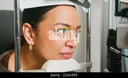 Giovane donna sottoposta a un esame oculistico presso un optometrista con apparecchiature avanzate Foto Stock