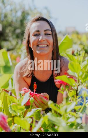 Una donna sorride e tiene in mano un fiore rosa. Concetto di felicità e appagamento, mentre la donna sta godendo la bellezza del fiore e. Foto Stock
