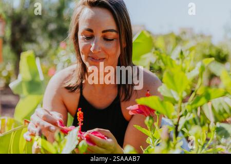Una donna si prende cura di un giardino di fiori, compreso un fiore rosa. Lei sorride e si sta godendo il suo tempo in giardino Foto Stock