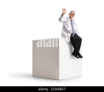 Medico maschio maturo seduto su un cubo bianco e ondulando isolato su sfondo bianco Foto Stock