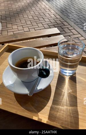 Tazza di espresso e bicchiere d'acqua su vassoio e tavolo in legno per esterni in formato verticale Foto Stock