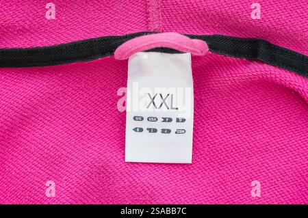 Etichetta per abbigliamento taglia XXL, tessuto bianco, isolata su rosa, primo piano dettagliato macro Foto Stock