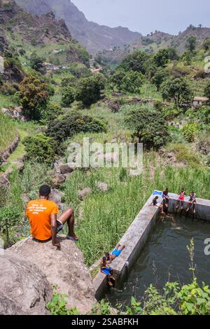 Un giovane su una roccia, osserva un gruppo di giovani intorno a uno stagno, nella verdeggiante valle di Paolo a Santo Antao, Capo Verde Foto Stock